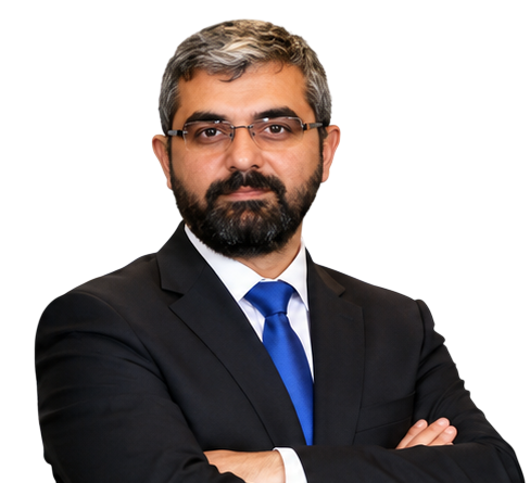 Mehmet Karaoğul, koyu renk takım elbisesi ve mavi kravatıyla, kollarını önde birleştirmiş halde